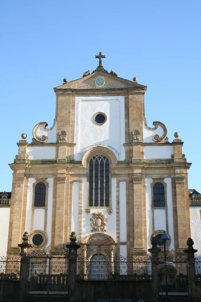 Barocke Fassade der Paderborner Marktkirche vor blauem Himmel, davor ein schmiedeeiserner Zaun